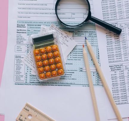 Magnifying glass, calculator, pencils on tax forms with pink background. Ideal for finance or education themes.